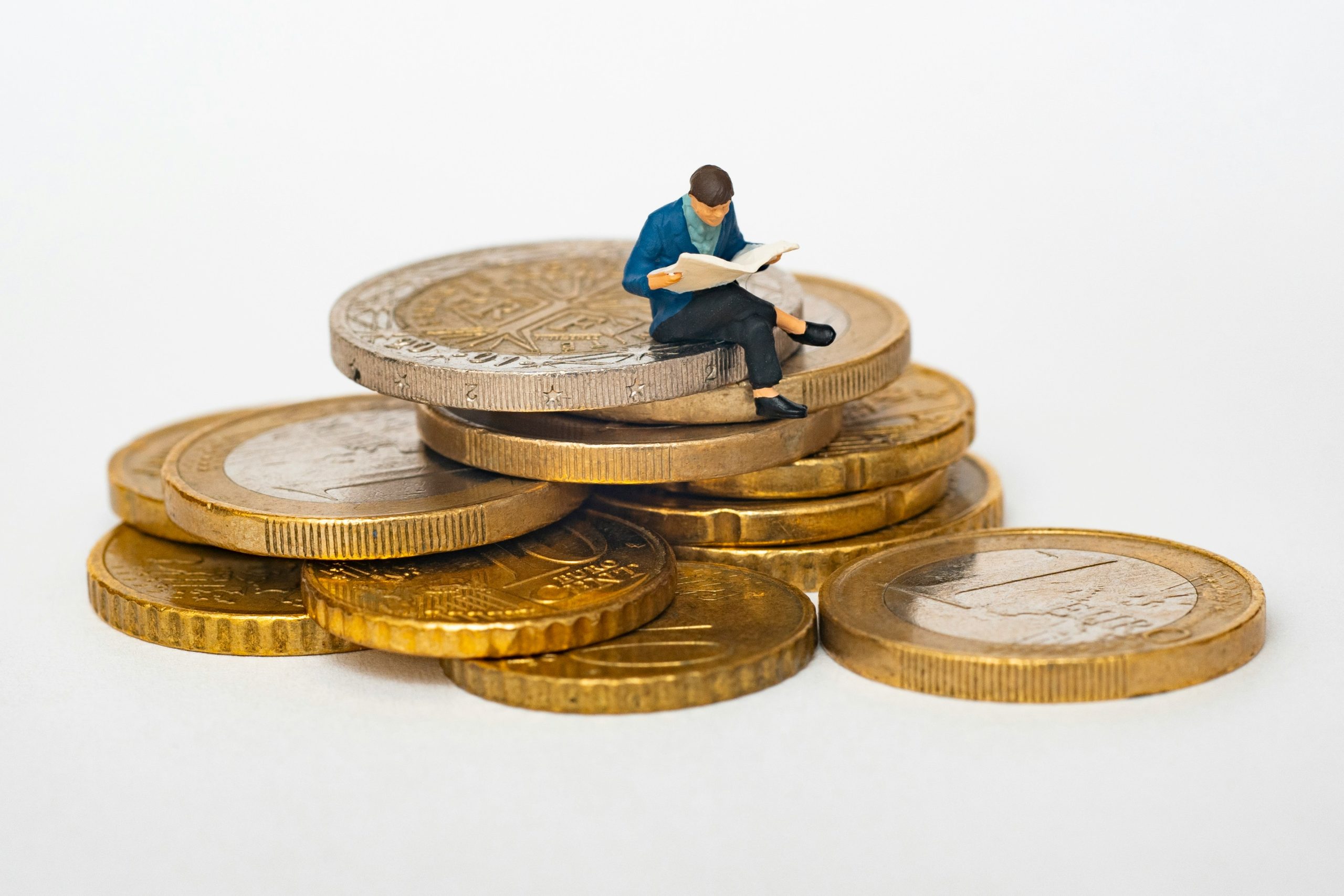 Una figura diminuta se sienta a leer un libro encima de una pila de grandes monedas de oro y plata, transmitiendo un concepto de riqueza, conocimiento y alfabetización financiera.
