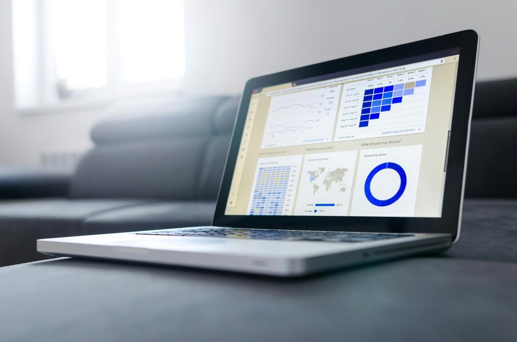 Una computadora portátil que muestra visualizaciones de datos, incluyendo gráficos y tablas, colocada sobre un sofá. Ambiente neutro con iluminación suave.