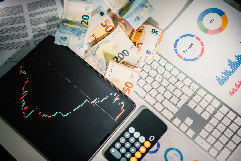 Tableta que muestra un gráfico de acciones, billetes de euro esparcidos, un teclado, una calculadora y gráficos de negocios en papel, transmitiendo un tema de análisis financiero.